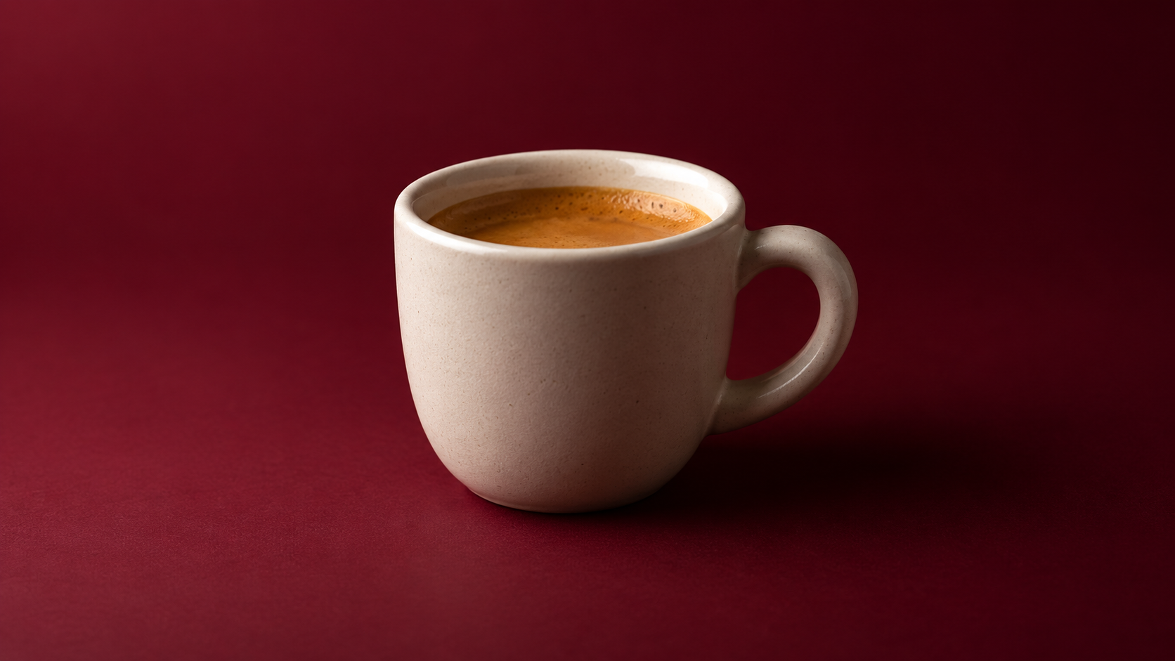 Uma xícara de café expresso em cerâmica fosca moldada por uma luz ampla e suave contra um fundo bordô.